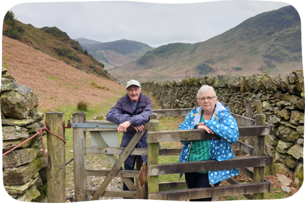 A couple leaning against a gate with hills in the background.