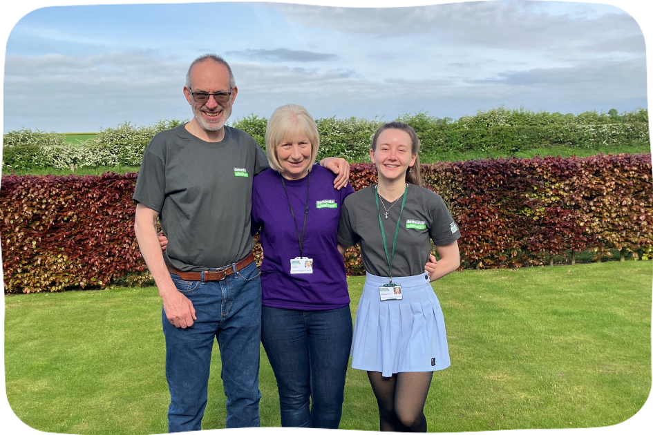 Three Dementia Adventure volunteers standing in Dementia Adventure t-shirts with their arms around one another.