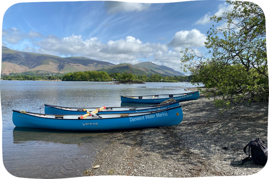 Two canoes on the bank of a lake with mountains in the background.