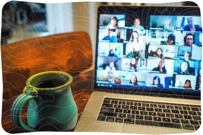 A laptop showing many people on a video call. A green mug sits beside the laptop.